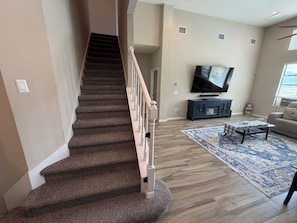 Una escalera conduce a una sala de estar con televisión de pantalla plana, un sofá y una mesa de centro.