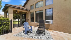 A house with a covered patio area, a blue Adirondack chair, a black folding chair, and a patterned rug.