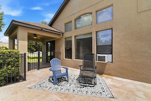 A house with a covered patio area, a blue Adirondack chair, a black folding chair, and a patterned rug.