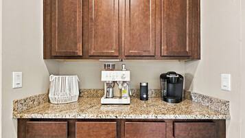 A kitchen with wooden cabinets, a coffee maker, a kettle, and a woven basket on the countertop.