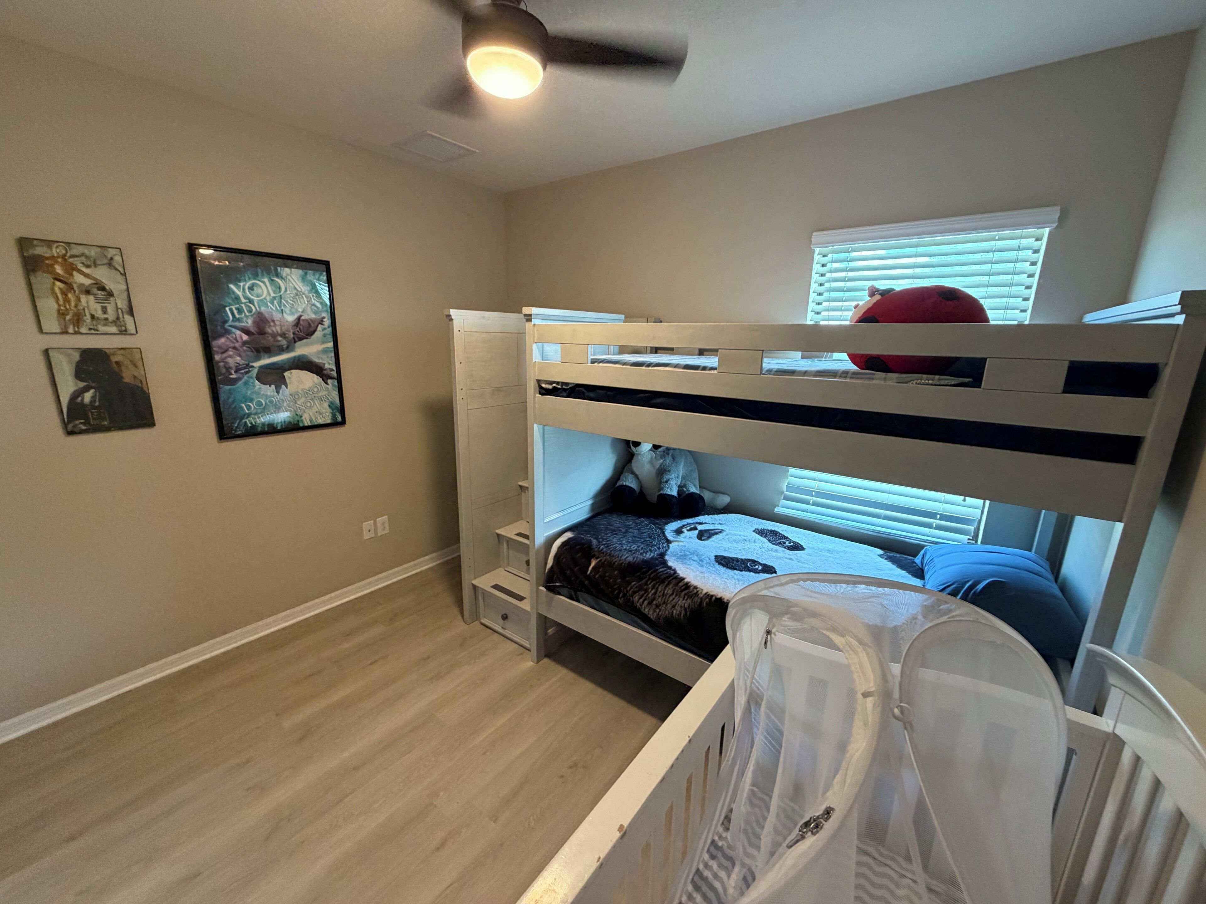 A bunk bed room with a ceiling fan, a window with blinds, and wall art.