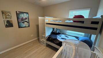 A bunk bed room with a ceiling fan, a window with blinds, and wall art.