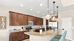 A modern kitchen with wooden cabinets, stainless steel appliances, a granite countertop, and pendant lighting.