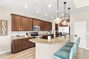 A modern kitchen with wooden cabinets, stainless steel appliances, a granite countertop, and pendant lighting.