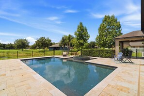 A rectangular swimming pool with a stone border, surrounded by a patio area with chairs and a small table. - Spacious 5BR Family Retreat w/ Private Pool & Spa (Plant City)