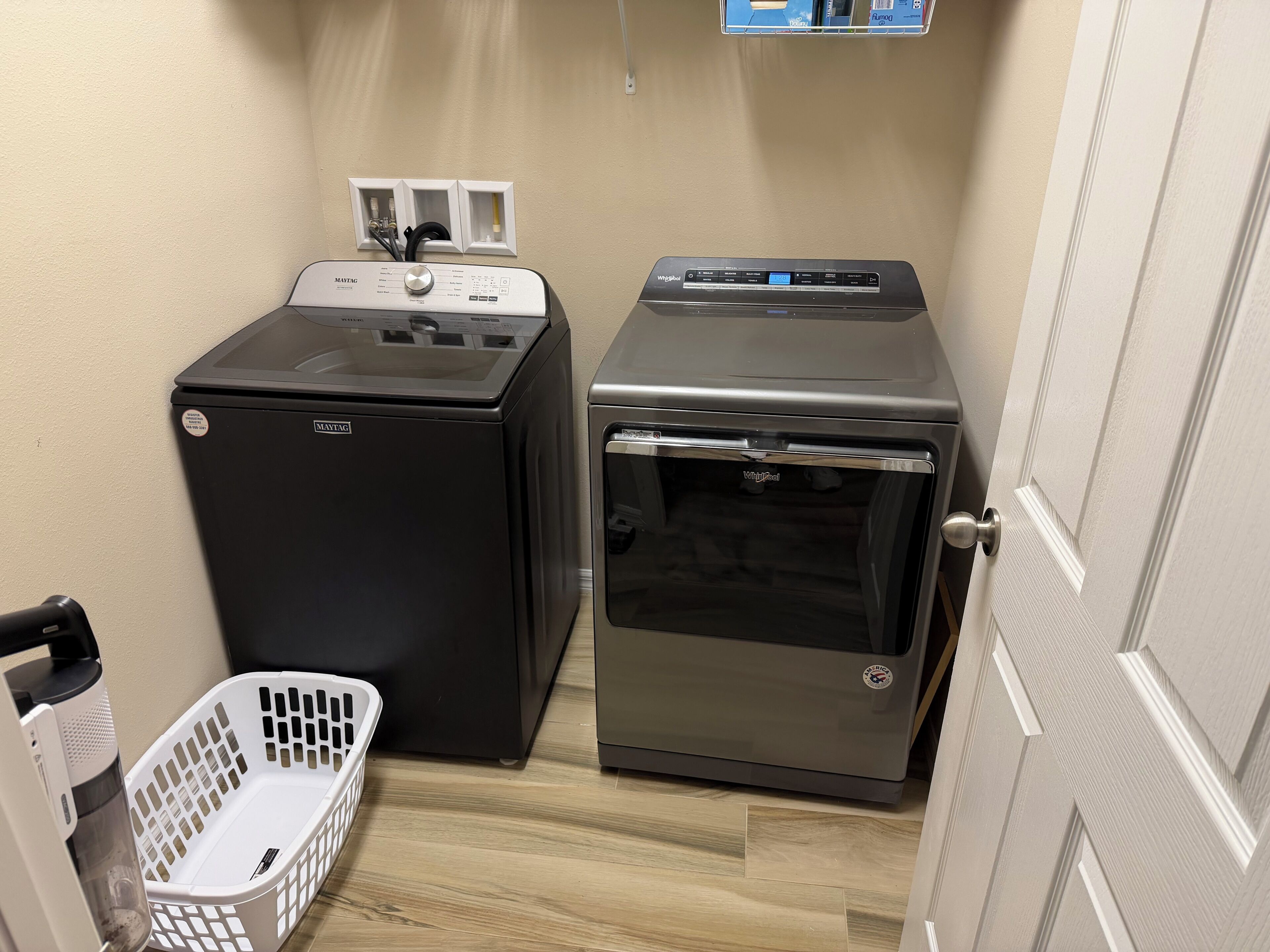 A compact laundry room with a black washing machine, a silver dryer, and a white laundry basket.