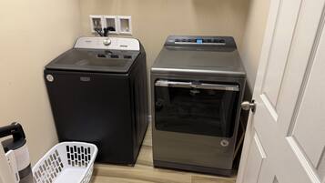 A compact laundry room with a black washing machine, a silver dryer, and a white laundry basket.