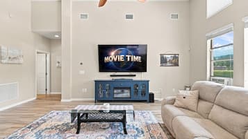 Ett vardagsrum med en platt-TV som är monterad på väggen, en blå TV-bänk, en beige soffa, en mönstrad matta och en takfläkt.