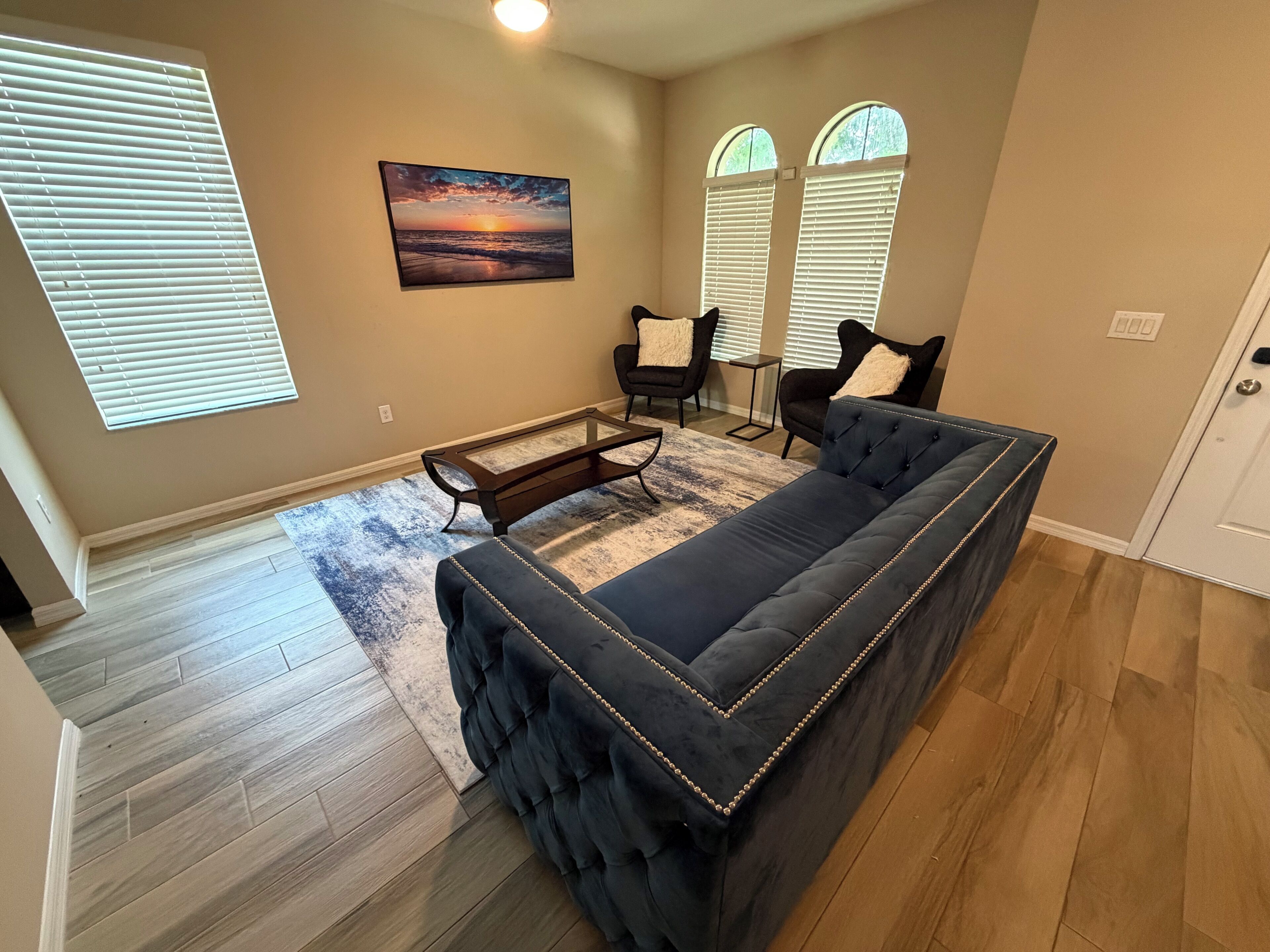 A living room with a sectional sofa, two armchairs, a coffee table, and a painting of a sunset.