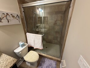 Ein Badezimmer mit einer Duschkabine, einer Toilette mit beigem Deckel, einem Handtuchhalter mit einem gefalteten Handtuch und einem Vogelgemälde an der Wand.
