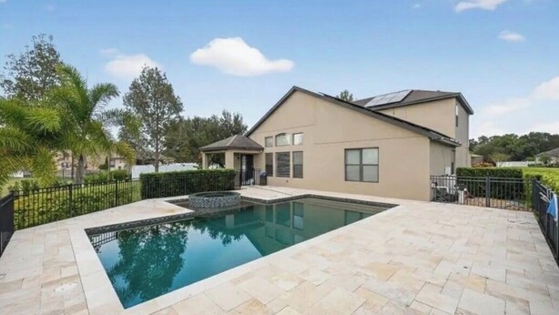 A modern house with a swimming pool, paved patio, and a small covered area.