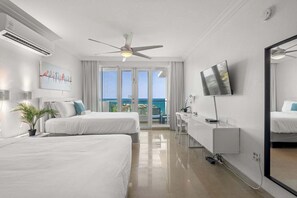 Ein Hotelzimmer mit zwei Betten, einem Schreibtisch, einem Fernseher und einem Balkon mit Meerblick.