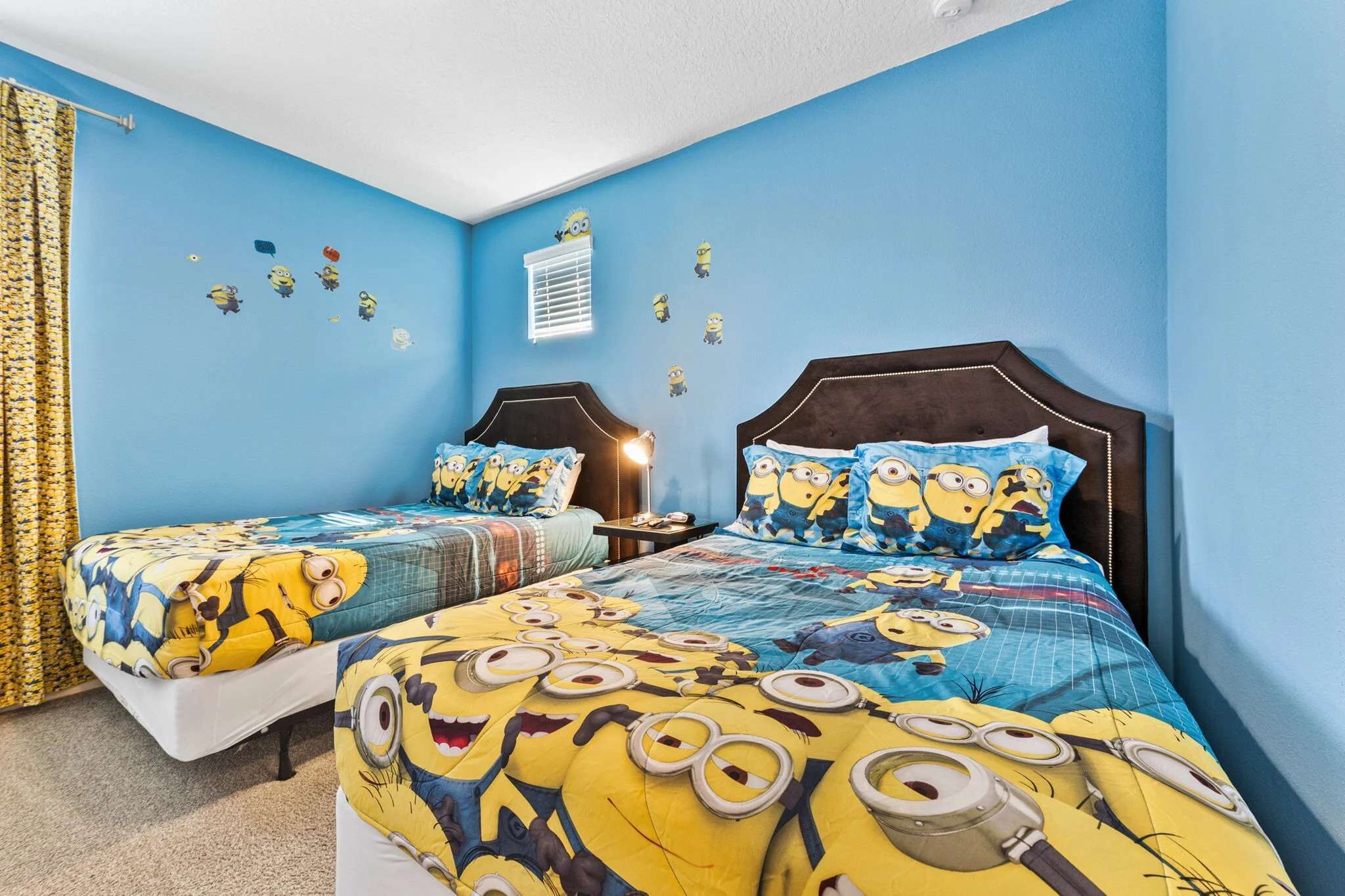 A bedroom with two beds, each with a blue wall and Minion-themed bedding.