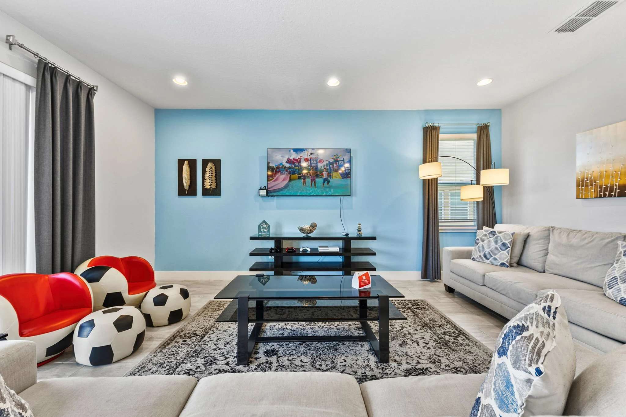 A living room with a sofa, a coffee table, and red and white chairs. There is a painting on the wall and a lamp on the side table.