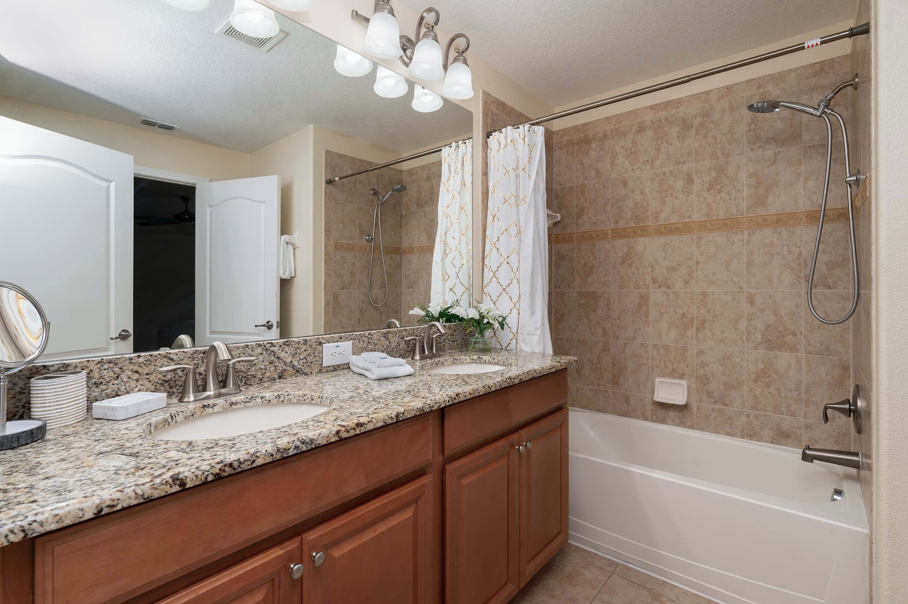 A bathroom with a double sink vanity, a large mirror, a shower with a handheld showerhead, and a towel rack.