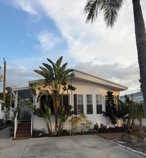 Une maison de plain-pied dotée d’un porche abrité, de grandes fenêtres et d’un jardin bien entretenu où poussent des plantes tropicales.