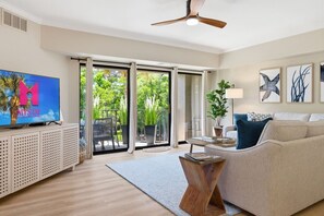 Ein Wohnzimmer mit Fernseher, Sofa, Couchtisch und einem Balkon mit Pflanzen.