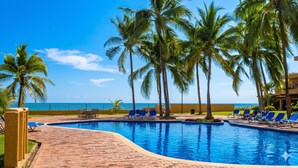 Zona de piscina con palmeras y vista al océano.