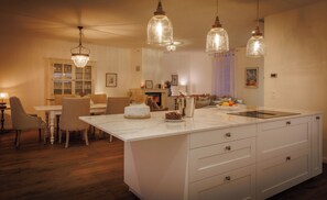 Une cuisine spacieuse dotée d’un îlot en marbre, de luminaires suspendus et d’un coin repas avec des chaises et une table.