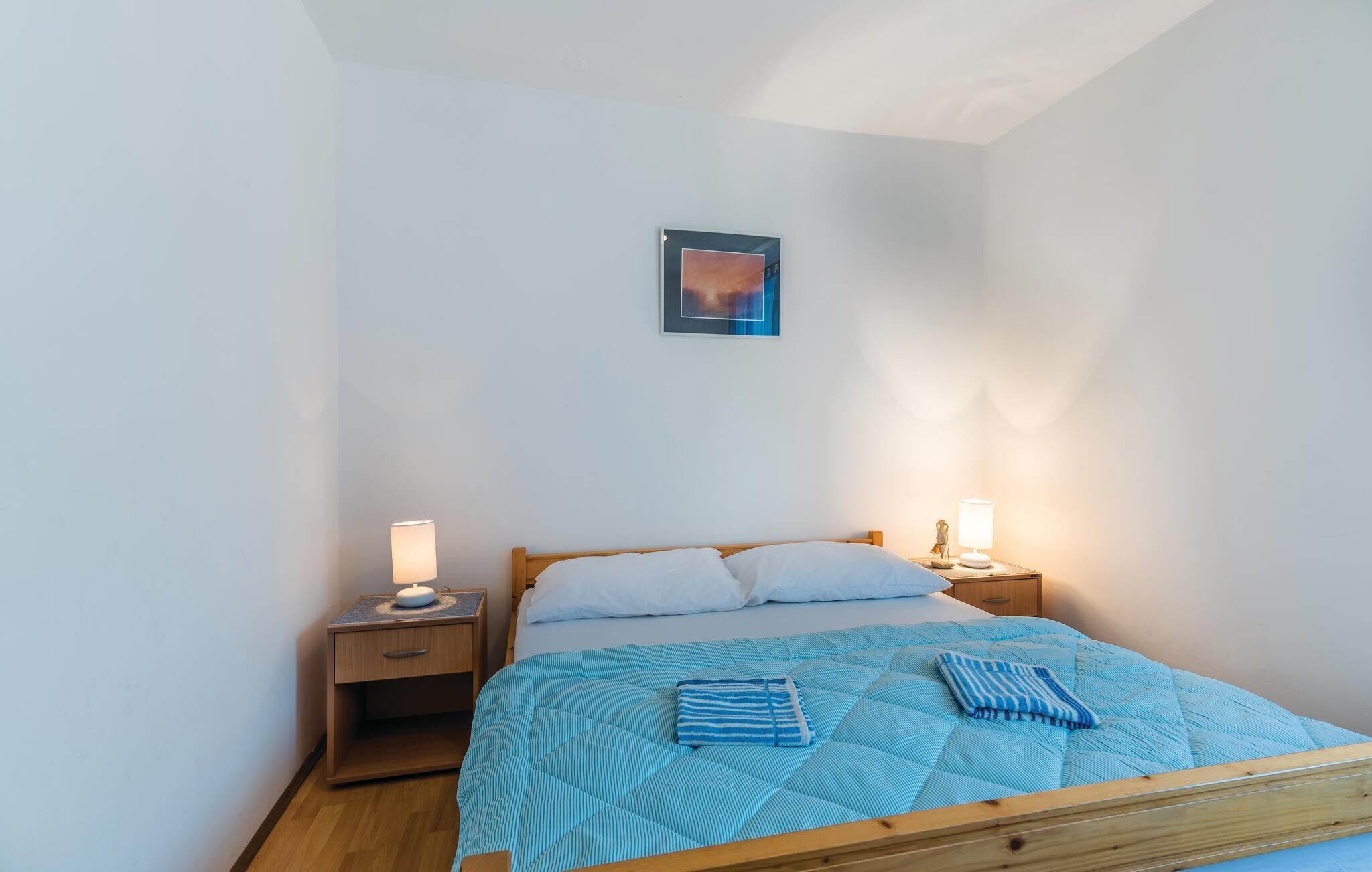 Une chambre à coucher avec un lit, deux tables de chevet avec des lampes, un tableau accroché au mur et une fenêtre.