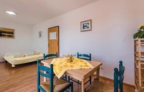 Ein Zimmer mit Holztisch, blauen Stühlen, einem Bett, einer Tür und einem Bild an der Wand.