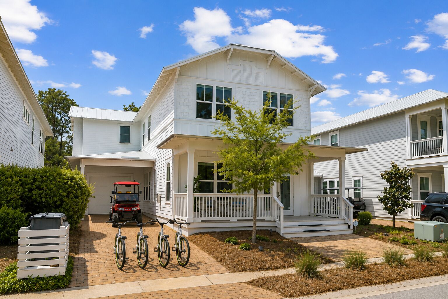 Une maison blanche à deux étages, dotée d’un porche abrité, d’un garage et d’un véhicule rouge garé à l’intérieur.