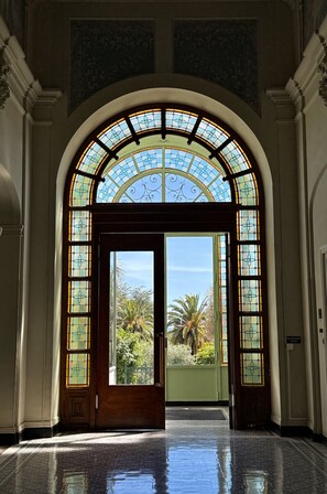 Ein spitzbogiges Portal mit Buntglasfenstern, das in einen Innenhof mit Palmen führt.