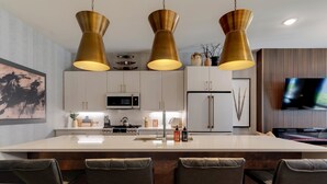 Een moderne keuken met een centraal eiland, roestvrijstalen apparatuur en hangende lampen.