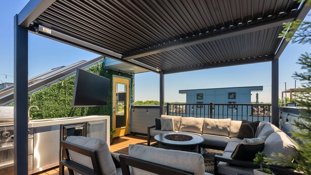 Een terras buiten met een barbecue, een zithoek en een televisie.