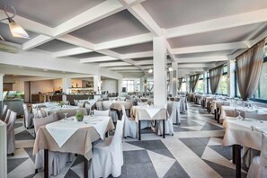 A spacious restaurant with multiple tables, a kitchen area, and large windows. - Atrium Hotel Halkidiki (Kassandra)