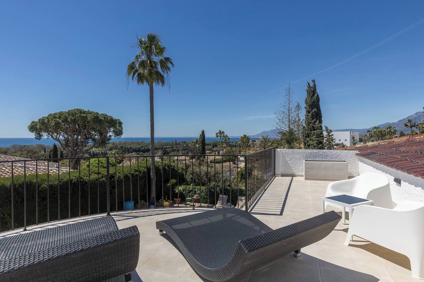 A rooftop terrace with outdoor furniture, a view of the sea, and a mountainous landscape.