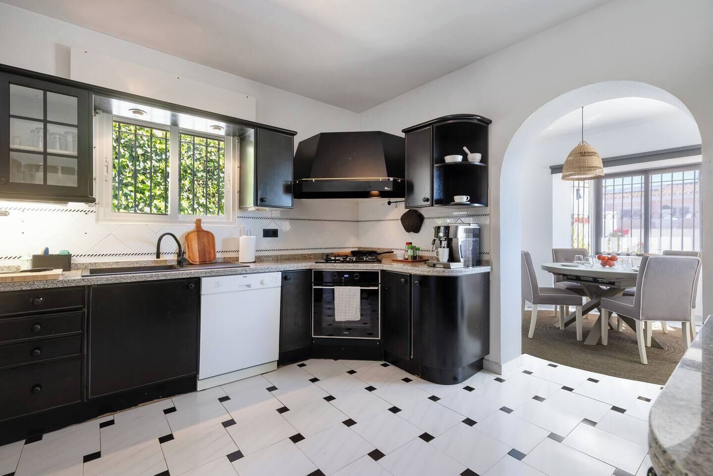 Een moderne keuken met zwarte kastjes, een vaatwasser, een oven en een eethoek met een tafel en stoelen.