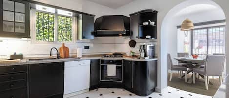 Een moderne keuken met zwarte kastjes, een vaatwasser, een oven en een eethoek met een tafel en stoelen.
