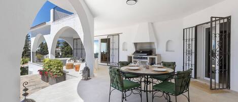 A modern outdoor dining area with a round table, green chairs, and a grill station.