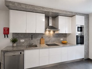 A modern kitchen with white cabinets, a stainless steel range hood, a built-in oven, and a dishwasher. - Luxury Mountain View Apartment in Machico (Machico)