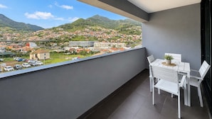 A balcony with a view of a town and mountains, a table with chairs, and a potted plant. - Luxury Mountain View Apartment in Machico (Machico)