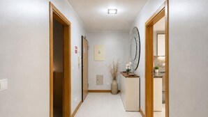 A hallway with wooden doors, a small desk with a vase, a mirror, and a clock on the wall. - Luxury Mountain View Apartment in Machico (Machico)