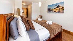A hotel room with a bed, a painting of a sunset, and a wooden headboard. - Luxury Mountain View Apartment in Machico (Machico)
