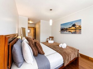 A hotel room with a bed, a painting of a sunset, and a wooden headboard. - Luxury Mountain View Apartment in Machico (Machico)