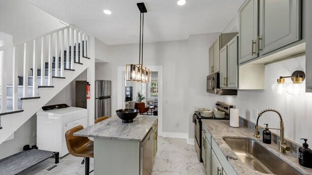 A modern kitchen with a marble island, stainless steel appliances, and a staircase with white railings. - The Dugout | Hot Tub (Columbia)