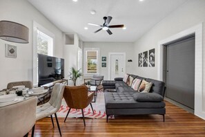 Uma sala de estar ampla com um sofá seccional grande, um espaço para refeições e um ventilador de teto.