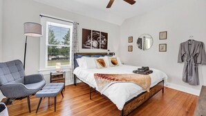 A bedroom with a bed, a chair, a standing lamp, a ceiling fan, and a window with blinds. - The Dugout | Hot Tub (Columbia)