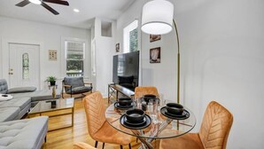 A modern living room with a sofa, a glass dining table set for four, and a ceiling fan. - The Scoreboard | Hot Tub (Columbia)