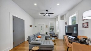 A modern living room with a grey sectional sofa, a TV, and a dining area with a table and chairs. - The Scoreboard | Hot Tub (Columbia)