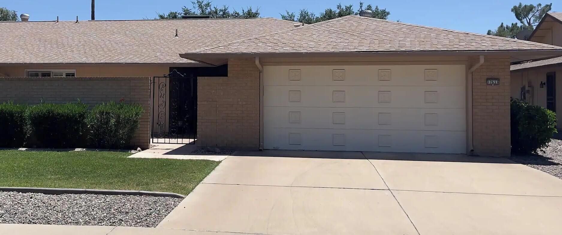 A residential garage with a beige exterior, a brick wall, and a clear driveway.