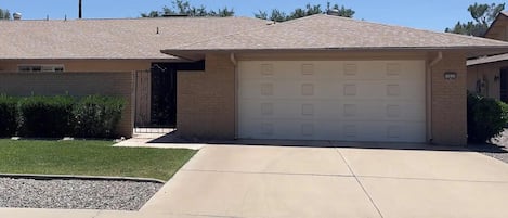 A residential garage with a beige exterior, a brick wall, and a clear driveway.