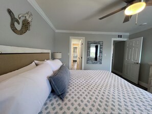 A bedroom with a bed, a nightstand, a lamp, a ceiling fan, a mirror, and a door.