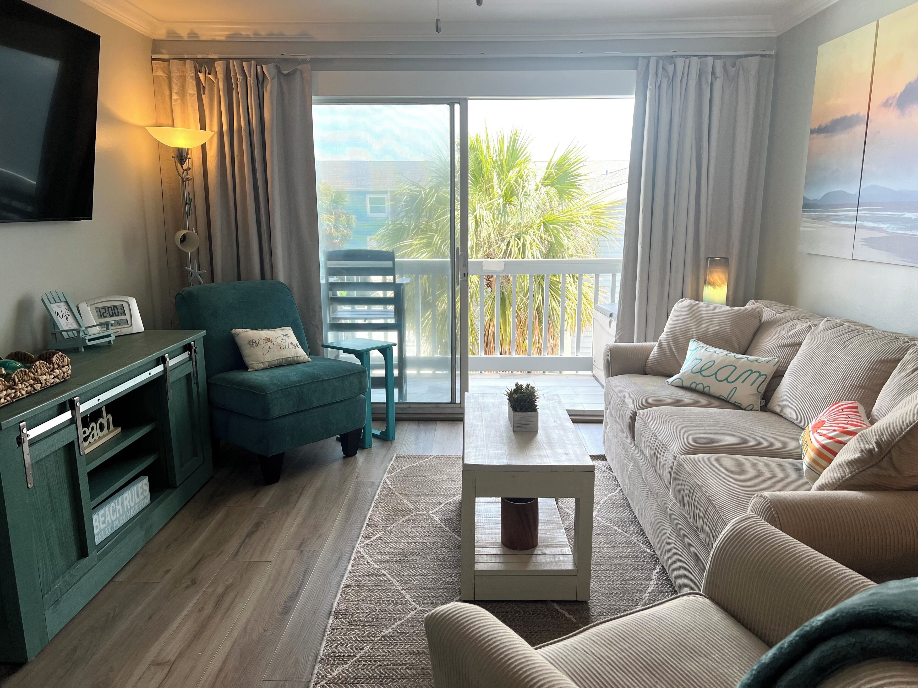 A living room with a sofa, armchair, coffee table, TV, and a balcony with a view.