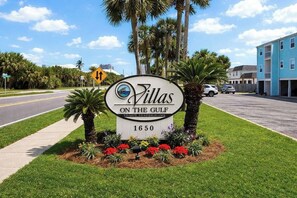 A sign for Villas on the Gulf with a number 1650, surrounded by palm trees and flowers.