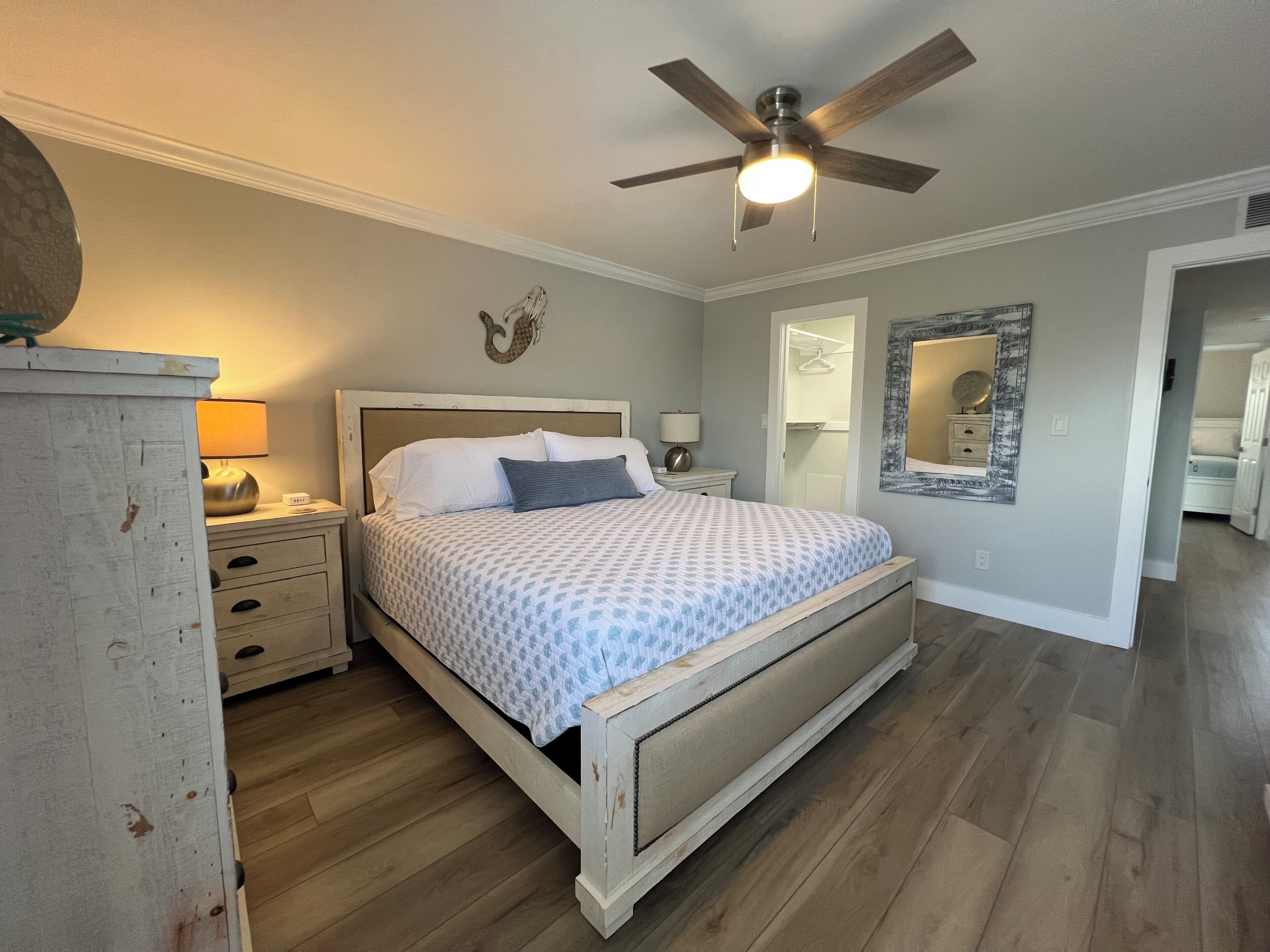 A bedroom with a bed, a ceiling fan, a nightstand, a dresser, and a mirror on the wall.